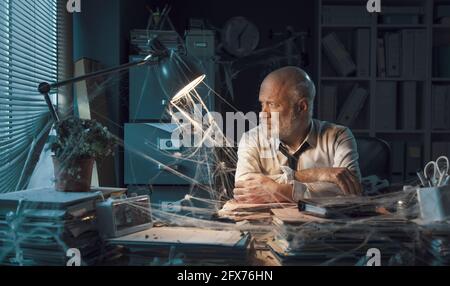 Uomo d'affari aziendale che si occupa di fallimento aziendale, è seduto alla scrivania nel suo ufficio polveroso abbandonato Foto Stock
