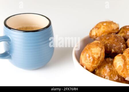 le chouquettes francesi puffs con perle di zucchero sul piatto con la tazza blu di caffè. Pasticceria Choux panetterie francesi classiche. Foto Stock