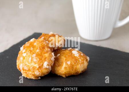 chouquettes francesi puffs con perle di zucchero su tavola nera di ardesia con tazza bianca di caffè. Panetterie francesi classiche Foto Stock