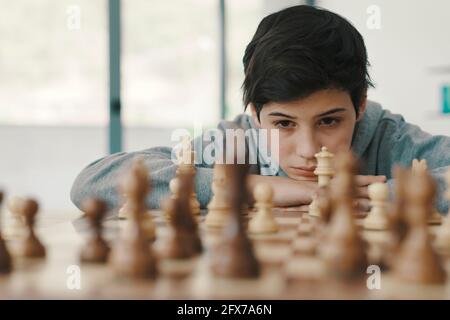 Giovane ragazzo intelligente che gioca a scacchi a casa, è concentrato e guardando la scacchiera Foto Stock