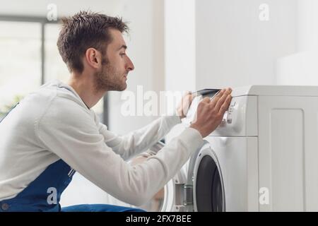 Riparatore che fissa una lavatrice, sta regolando una manopola sul pannello di controllo Foto Stock