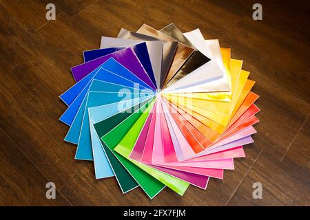 Pila attorcigliata di 12x12 fogli colorati di carta adesiva su sfondo marrone. Colori assortiti. Foto Stock