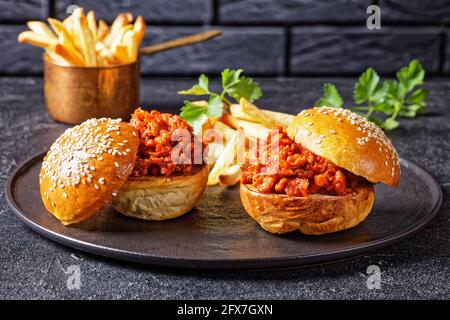 Panini Sloppy Joe con patatine fritte su un piatto nero con un muro di mattoni sullo sfondo, primo piano, cucina americana Foto Stock