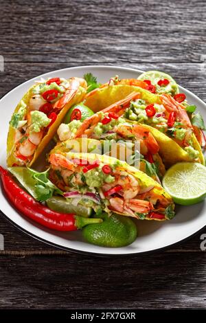 conchiglie di taco con gamberi alla griglia, insalata di cavolo, lime e guacamole su un piatto su un tavolo di legno Foto Stock