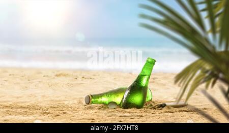 Dettaglio di bottiglie di birra fresca a metà sepolta nella sabbia su una spiaggia con foglie di palma in una giornata calda. Dettaglio della vista frontale. Foto Stock