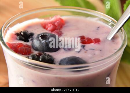 Macro di tazza di vetro con yogurt con frutti di bosco con metallo cucchiaio su tavolo di legno Foto Stock