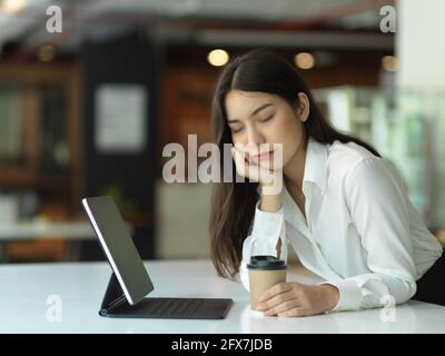 Ritratto di operaio femminile offie occhi chiusi sentirsi rilassato e. tenere una tazza di caffè mentre si è seduti alla scrivania dell'ufficio Foto Stock