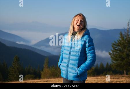 Ritratto di una donna felice in piedi sullo sfondo di colline di montagna ricoperte di nebbia e sorridente. Al mattino potrete respirare l'aria fresca di montagna sotto il cielo blu del sole. Foto Stock