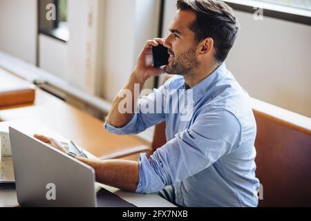 Uomo che parla al telefono cellulare alla scrivania in ufficio. uomo d'affari seduto alla scrivania e che parla con uno smartphone. Foto Stock