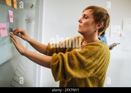 Dirigente donna che mette appiccicosa nota sul vetro. donna d'affari che incolla una nota adesiva sul vetro per la strategia di pianificazione. Foto Stock