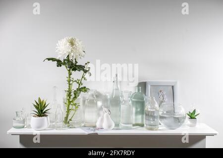 il crisantemo bianco in vaso di vetro con bottiglie di diverse forme con acqua si trova sulla cassettiera. Spazio di copia Foto Stock