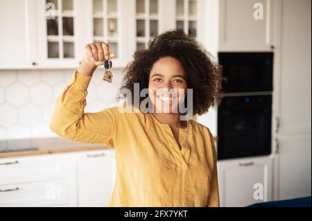 Felice eccitato afroamericana donna che tiene le chiavi in mano, sopravorato con l'acquisto della propria proprietà. Donna allegra si è ricollocata in un nuovo appartamento, affittare una casa. Concetto di obiettivo di raggiungimento Foto Stock