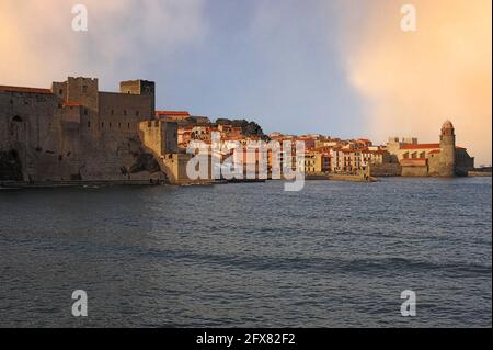 Il lungomare della città vecchia a Collioure, Pyrénées-Orientales, Occitanie, Francia. Sulla sinistra si trova il Château Royal (Castello reale), fondato dai Cavalieri Templari nel 1207, convertito più tardi nello stesso secolo per ricevere la corte dei Re di Maiorca, e occupato dagli spagnoli fino al 1642. Sulla destra si trova il campanile dell'Église Notre-Dame-des-Anges (Chiesa di nostra Signora degli Angeli), costruito inizialmente come faro medievale di pharos. Il faro, ora sormontato da una cupola rosa in stile toscano, segnalava la posizione dell’antico porto commerciale alle navi in mare con fumo di giorno e fuoco di notte. Foto Stock