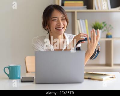 Ritratto di una donna felice che tiene le cuffie e ride mentre lavora in sala ufficio Foto Stock