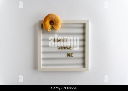 Letterboard con parole che Spell Donut Giudice Me, con una ciambella fresca, in lettere dorate, su sfondo bianco, orizzontale Foto Stock