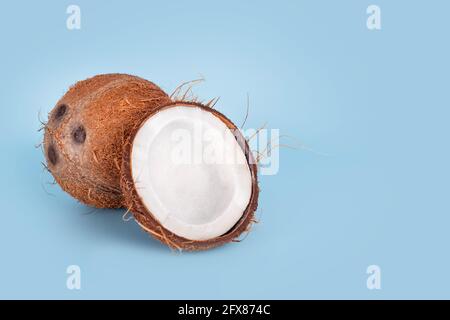 Noci di cocco intere e incrinate su sfondo azzurro. Frutta di cocco sbucciata che mostra i tre pori caratteristici. Tagliare a metà la chiocciola di cocco. Foto Stock