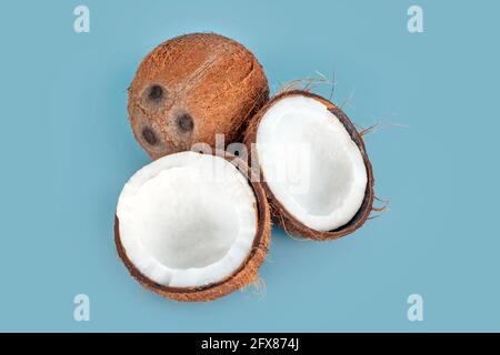 Noci di cocco intere e incrinate su sfondo azzurro. Frutta di cocco sbucciata che mostra i tre pori caratteristici. Tagliare a metà la chiocciola di cocco Foto Stock
