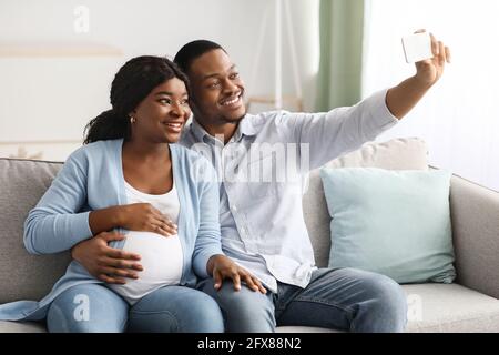 Positivo incinta famiglia nera che prende selfie, utilizzando smartphone Foto Stock