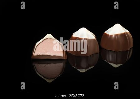 Caramelle al cioccolato su sfondo scuro con riflessi. Pezzo per pezzo e nel complesso. Ripieno di frutta e frutta. Spazio di copia. Foto Stock