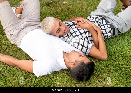 Giovane coppia gay latino-americana sdraiata sull'erba in un parco. Foto Stock