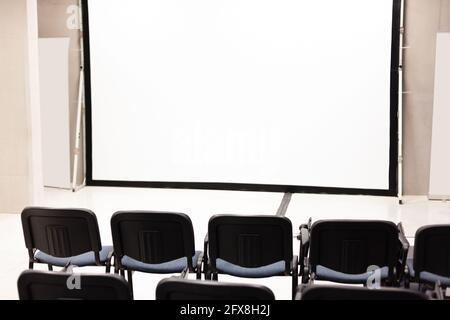 File di sedie da ufficio davanti a uno schermo vuoto per presentazioni multimediali aziendali, interno di una sala conferenze vuota, auditorium vuoto, eventi pubblici, ecc. Foto Stock