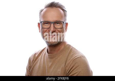 Sorridente amichevole unshaven uomo di mezza età in leisurewear indossare occhiali girando per guardare la fotocamera in un ritratto della parte superiore del corpo su bianco Foto Stock