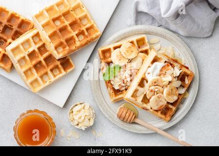 Colazione con waffle belgi con banana, yogurt e mandorle, vista sul tavolo. Cialde dolci da dessert Foto Stock
