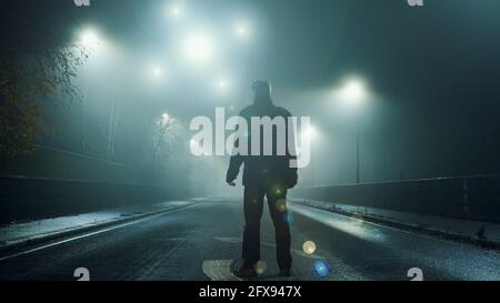 Un concetto UFO di orbs incandescenti, galleggianti sopra una strada degli inverni nebbiosa di notte. Con una figura silhouette , torna alla fotocamera, guardando le luci. Foto Stock