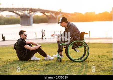 un uomo in sedia a rotelle cammina con l'amico. Uomo che cammina con un amico disabili in sedia a rotelle al parco Foto Stock