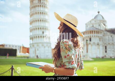 Felice giovane donna in abito floreale con pizza e cappello vicino alla Torre Pendente di Pisa, Italia. Foto Stock