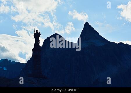 Statua e vetta di montagna in serata al Passo del Gran San Bernardo collega Martigny nel Cantone Vallese, Svizzera con Aosta, Italia Foto Stock