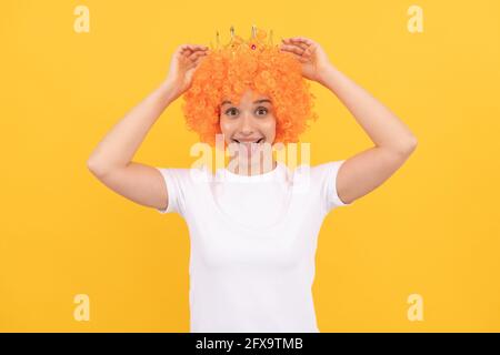 felice egoista divertente ragazza con look fantasia indossando parrucca capelli arancio e principessa corona, vincitore Foto Stock