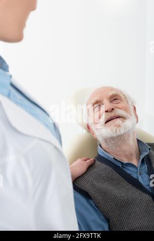 sorridente paziente anziano sdraiato in sedia dentale con la mano del dentista sulla spalla Foto Stock