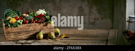 Pere dolci e foglie essiccate poste su tavola di legno vicino scatola con varie verdure fresche contro parete grigia di shabby Foto Stock