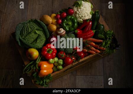 Da sopra cassa con verdure mature assortite messe su legno pavimento in camera oscura Foto Stock