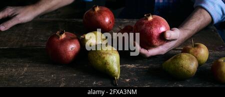 Ampio angolo di uomo anonimo che porta frutta matura su legname tavola rustica con melograni e pere Foto Stock