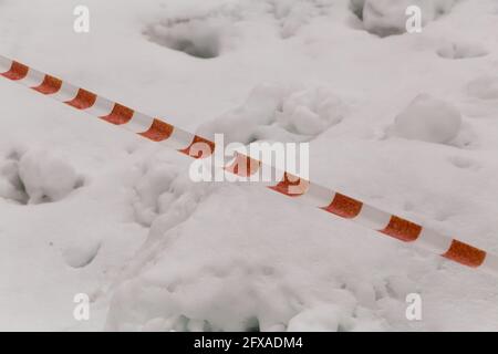 Il nastro bianco-rosso a strisce di segnale viene allungato diagonalmente. Il passaggio è chiuso in un'area pericolosa del terreno. Area recintata dall'ingresso della gente. Foto Stock