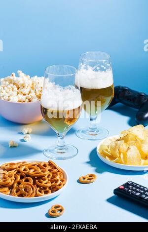 Bicchieri di birra leggera, spuntini su sfondo blu con un telecomando dal TV, un joystick dalla console di gioco. Foto Stock