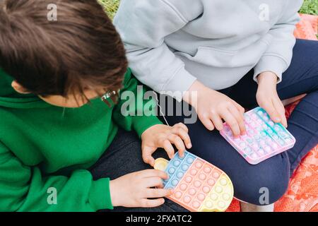 Ragazzi e bambine che giocano colorful poppit sensoriale gioco. Primo piano di mani di bambini che spingono multi colorful trendy pop IT bolla flessibile fidget giocattolo. ANX Foto Stock