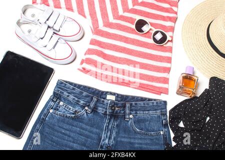 look estivo: camicia a righe, tablet, pantaloncini in denim, cappello di paglia, occhiali da sole e scarpe da ginnastica isolate su bianco. Foto Stock