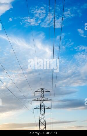 Pilone e cavi elettrici contro un blu nuvoloso e luminoso cielo che fornisce elettricità domestica alle case per il fabbisogno di energia verde Foto Stock