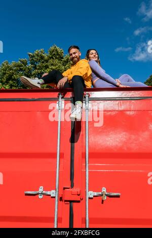 Coppia sorridente seduta indietro su un contenitore rosso Foto Stock