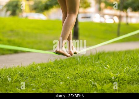 Giovane donna che equilibrano a piedi nudi su slackline nel parco pubblico Foto Stock