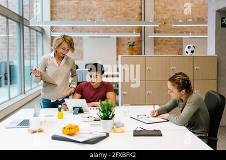 Imprenditrice femminile che assiste il giovane collaboratore maschile durante l'incontro in carica Foto Stock