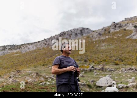Uomo anziano in piedi con binocoli in montagna Foto Stock