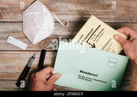 Mano mettendo il ballottaggio per le elezioni federali in busta sul tavolo con maschera protettiva e corona test rapido Foto Stock