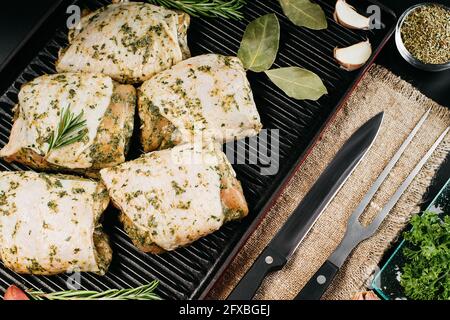 Cosce di pollo crude in marinata bianca con spezie fresche al rosmarino. Carne per grigliare e barbecue. Cosce di pollo crudo su sfondo scuro. Foto Stock