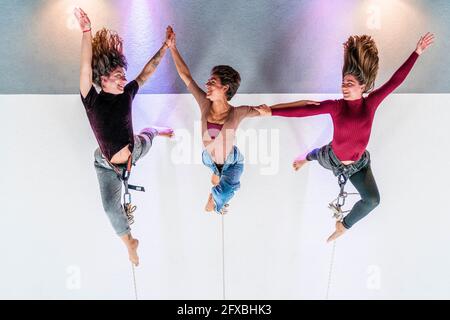 Danzatrice sorridente che tiene le mani mentre pende sulla corda in studio di danza Foto Stock