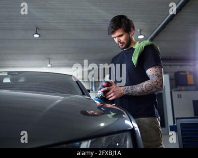 Uomo meccanico lucidante auto cofano in garage Foto Stock