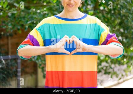 Donna mid adult che indossa la parte superiore multicolore che fa la forma del cuore nel giardino Foto Stock